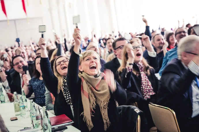 Begeistertes Publikum an Tischen interagiert mit Signalkellen.